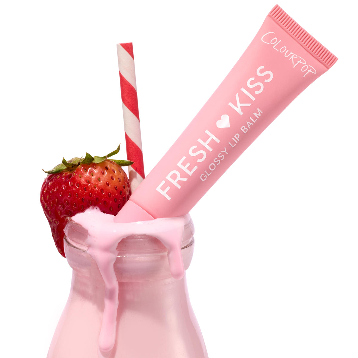 Pink tube of ColourPop Fresh Kiss Glossy Balm in Strawberry Milk leaning in a glass bottle of strawberry milk, with creamy drips, a red-and-white striped straw, and a ripe strawberry, on a clean white background.