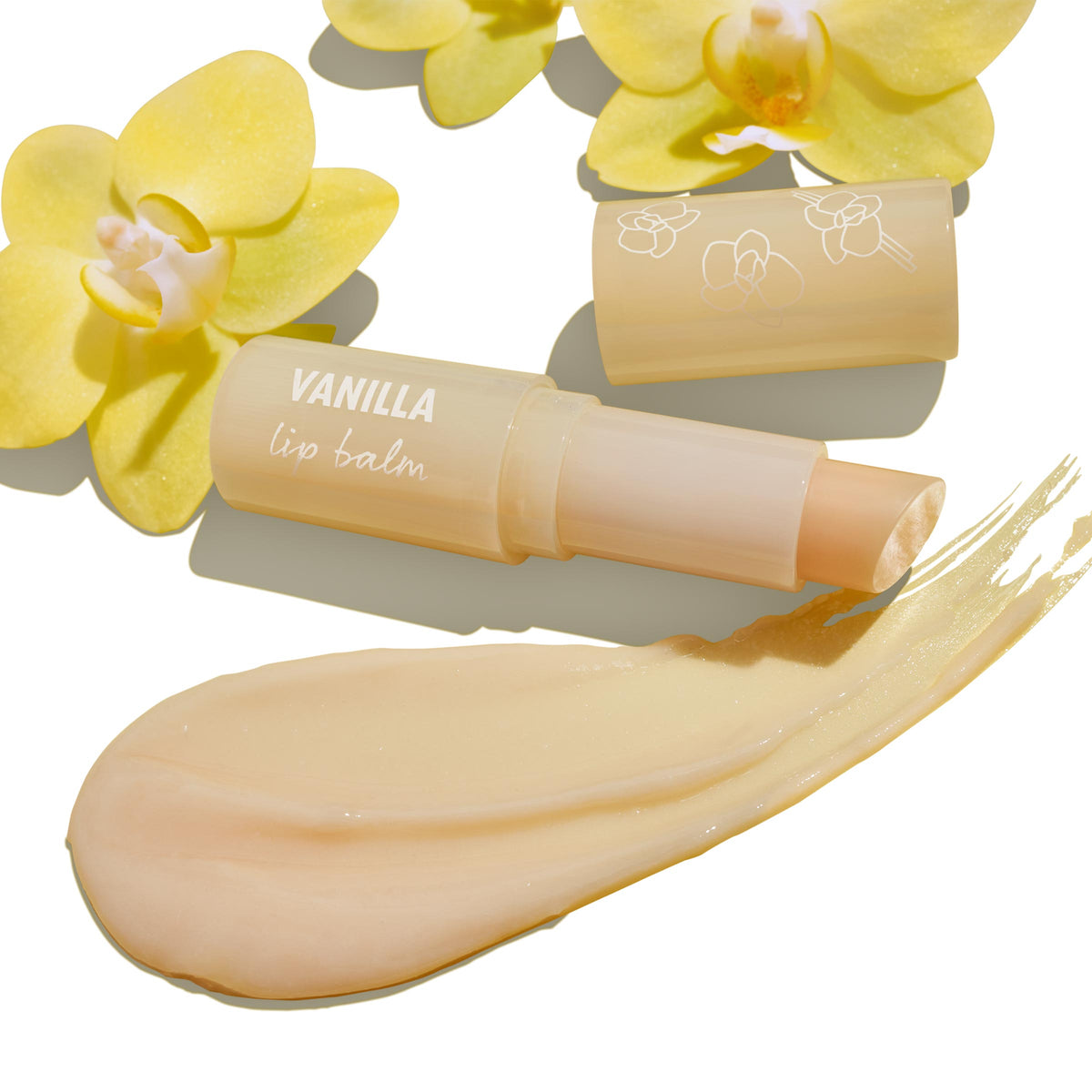 ColourPop Vanilla Lip Balm glides open to reveal a creamy beige stick with a glossy swatch, paired with an orchid-printed cap and yellow orchid flowers on a white backdrop, showcasing a hydrating, subtly tinted formula.