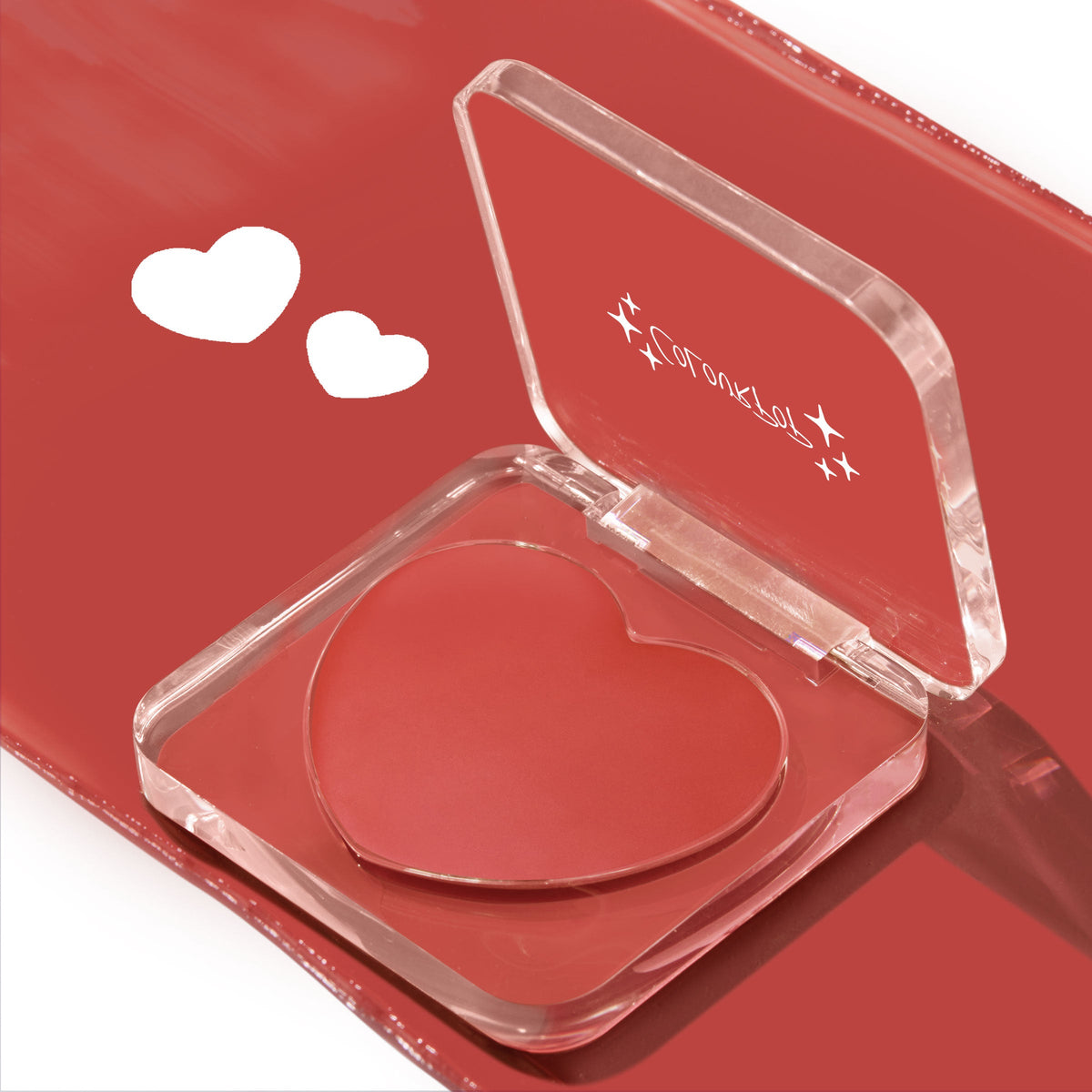 Heart-shaped pan of Second Date ColourPop Lip and Cheek Balm sits open in a clear compact, revealing a rosy red cream shade on a glossy matching red background with two white heart icons.