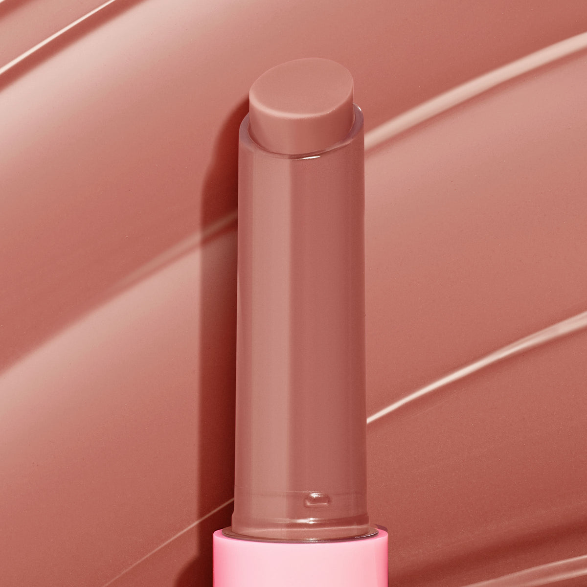 ColourPop So Juicy Plumping Gloss Balm with Peptides in Doe stands uncapped, twist-up stick revealing a creamy warm nude-brown tint, set against matching glossy swipes, in a pink tube for a plumping, glossy finish.