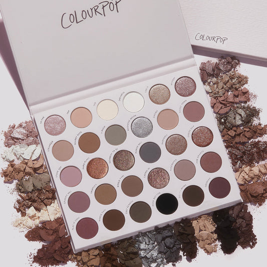 Stone Cold Fox ColourPop Shadow Palette lying open, displaying 30 cool‑toned neutral eyeshadows in matte and shimmer finishes; taupe, mauve, gray and champagne pans ringed by crushed powder swatches on a light backdrop.