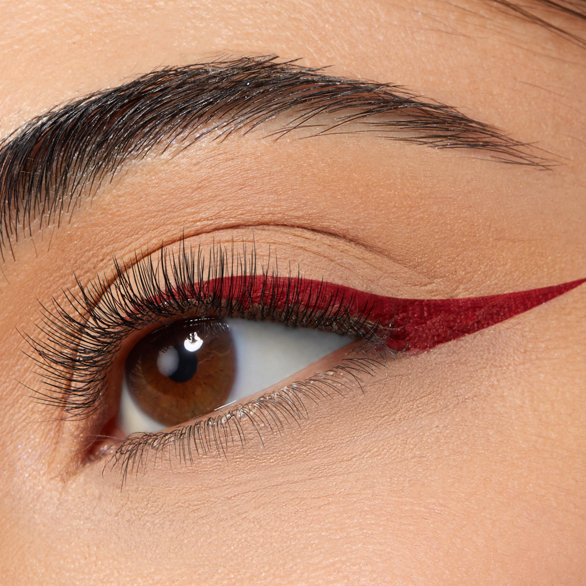 Wine-red winged eyeliner shapes a brown eye, a sharp cat-eye along the upper lash line created with ColourPop BFF Liquid Liner in Try Me; smooth matte lid and long lashes shown in a close-up.