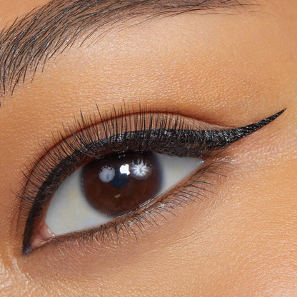 Sharp black cat-eye wing defining the upper lash line, applied with ColourPop BFF Liquid Liner in Numero Uno, on a close-up brown eye with natural lashes and smooth skin.