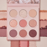 Blush Crush ColourPop Shadow Palette lies open, displaying a 9-pan range of rosy nude mattes and shimmers - Lovesick, Pop a Bottle, The One, Enamored, Made U Blush, Blossom Up, How Rouge, Cheek2Cheek, Blush Wine - with swatches streaked across a blush-pink backdrop.