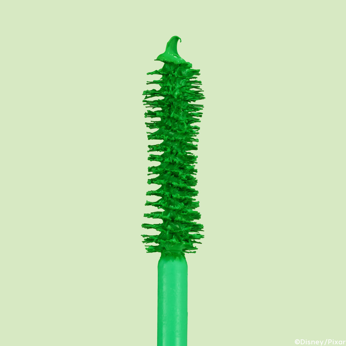 ColourPop BFF Mascara Roar! wand stands upright, bristles packed with vivid green formula and a small bead at the tip, showcasing the volumizing brush detail in a macro close-up against a pale mint background.