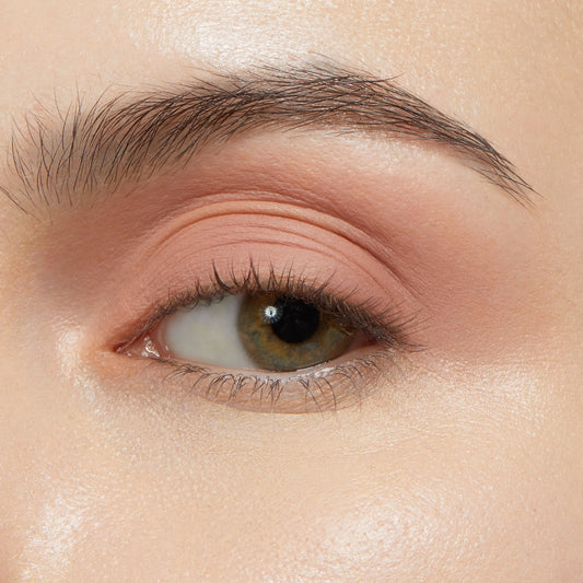 Eyelid wearing ColourPop Shadow Stix in Bare With Me, a soft peach nude eyeshadow stick, blended smoothly across the lid for a matte, crease-free finish, shown in close-up with natural lashes under studio lighting.