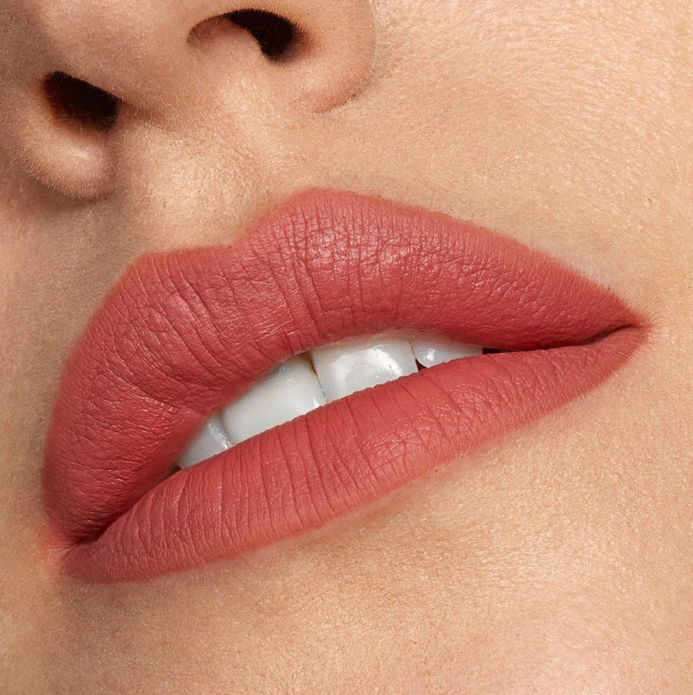 Close-up lips wear Brink, a ColourPop Lippie Stix, showing a warm dusty rose terracotta shade with a soft-matte, full-coverage finish; mouth slightly parted to reveal teeth, highlighting smooth texture against natural skin.