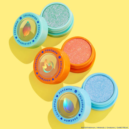 Flamethrower ColourPop Super Shock Shadow displays a sparkling coral-orange pan in an orange pot with a holographic flame lid, set on a bright yellow flat lay beside mint and sky-blue Pokémon-themed shadows.