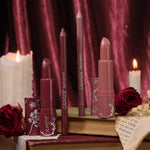Secret Kiss ColourPop Lipstick & Lip Pencil Set - two creamy lipsticks and two matching lippie pencils in deep berry and rosy nude - standing upright in floral-print tubes on vintage books amid roses and lit candles, burgundy velvet backdrop.