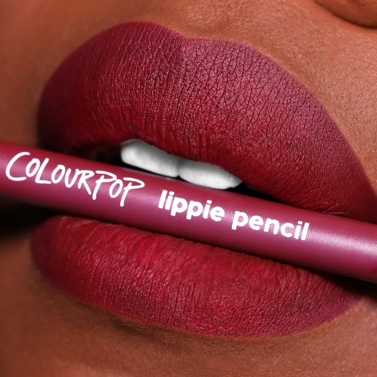 ColourPop Lippie Pencil in On Ice held between matte, berry-red lips, showcasing precise lip definition; mauve pencil with white logo in a tight beauty close-up, highlighting the liner's rich pigment and velvety matte finish.