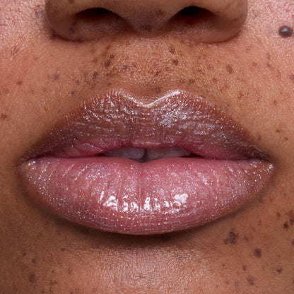 Close-up of freckled lips wearing Bright Ariel Ultra Glossy Lip, a shimmery pink Disney Princess lip gloss with high-shine, reflective sparkle and smooth, hydrated finish on medium skin tone.
