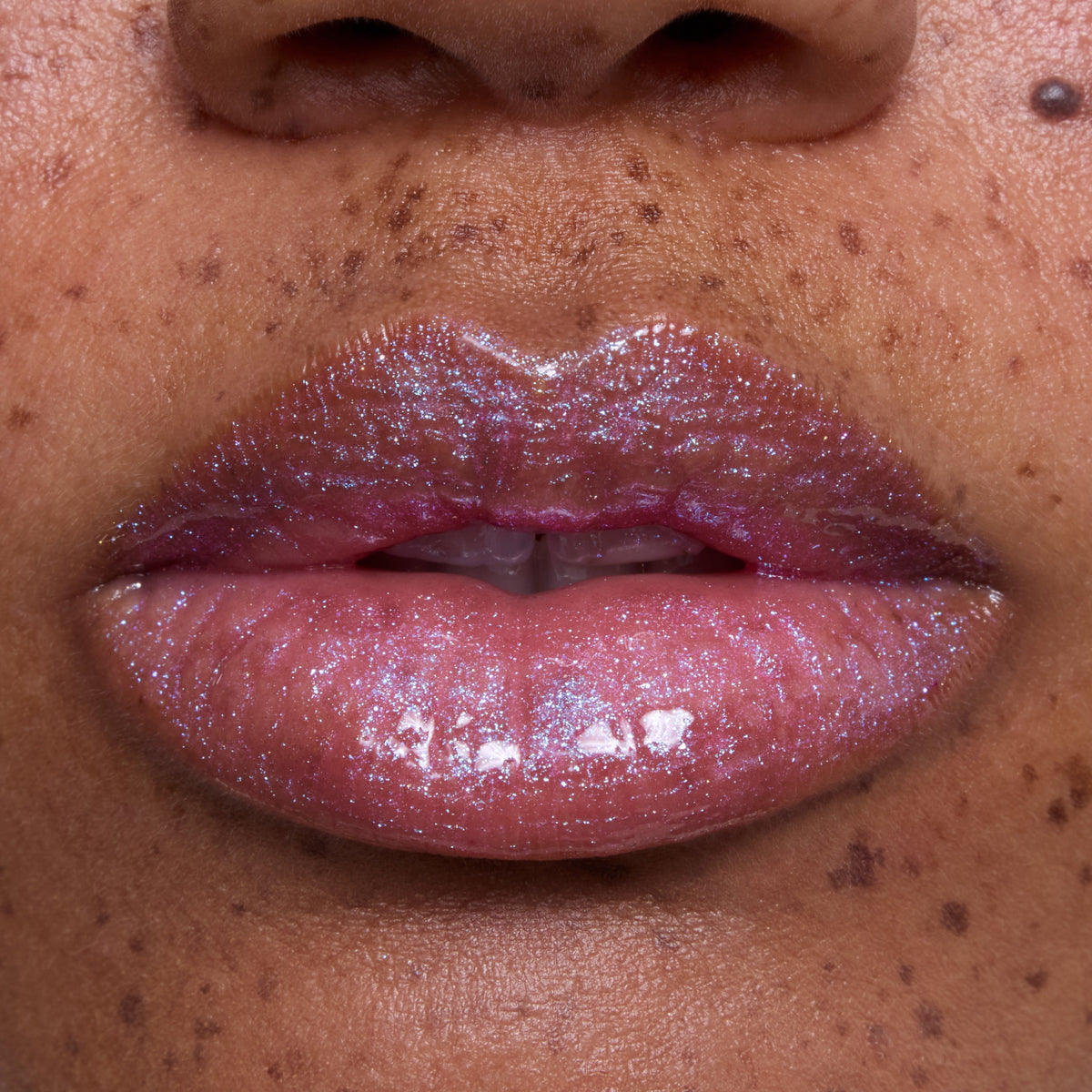 Close-up of freckled lips wearing Courageous Rapunzel Ultra Glossy Lip, a shimmering pink-lilac Disney Princess lip gloss with high-shine, iridescent sparkle on medium skin tone, showing smooth, hydrated finish and vivid color payoff.