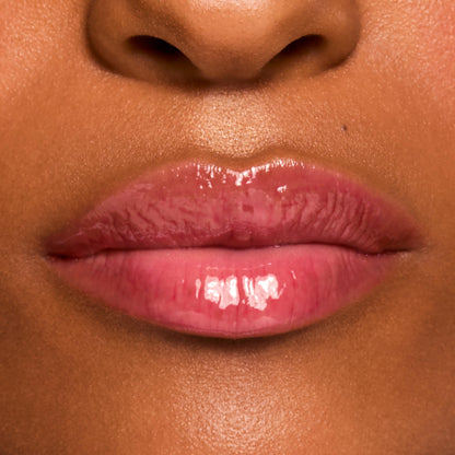 Glossy pink lips wearing a shade from the Fruit Basket ColourPop Glossy Lip Balm Trio, showing a sheer tint and high-shine, hydrated finish in a tight macro close-up on medium-brown skin.