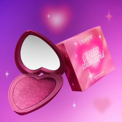 Heart to Get Cuter than Cupid Super Shock Blush compact showing a shimmery hot pink heart-shaped blush and built-in mirror beside its pink gradient box on a glowing purple background with soft starbursts, styled for US beauty shoppers.