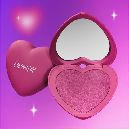 Cuter than Cupid Super Shock Blush in a heart-shaped ColourPop compact sits open to reveal shimmering pink pigment and built-in mirror against a glowing purple gradient backdrop, showcasing the Heart to Get romantic makeup collection.
