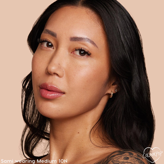 Model wearing Medium 10 N, showcasing a natural, dewy finish from ColourPop Pretty Fresh Tinted Moisturizer; close-up face with a neutral undertone against a soft peach background, minimal makeup for everyday wear.