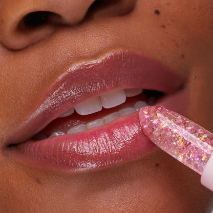 ColourPop pH Lip Balm Sing glides onto lips as a crystal-clear pink stick with iridescent flakes, delivering a glossy, rosy tint; close-up of mouth and teeth showcases hydrated shine and a subtle color-changing finish.