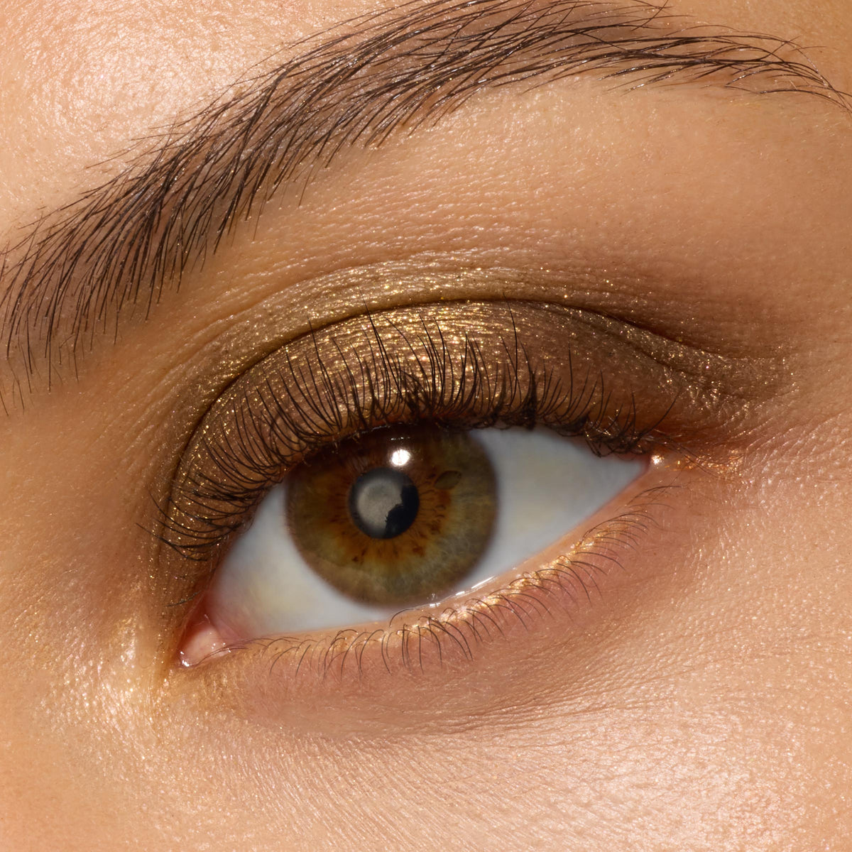 Shimmering antique-gold eyeshadow coats a single eyelid, blended into a warm bronze haze at the outer corner, showcasing ColourPop Super Shock Shadow We Won't Bite with a smooth metallic, cream-to-powder finish in a macro beauty swatch.