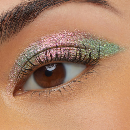 Close-up of a brown eye wearing Colourpop Galaxy Shadow Stix, showing a smooth swipe of metallic duochrome pink-to-green shimmer eyeshadow across the lid for a bold, iridescent makeup look.