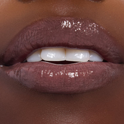 Glossy lips wearing ColourPop Ultra Glossy Lip in Noble Steed, a deep mauve-brown shade, shining with a high-shine finish and smooth, even coverage; close-up beauty swatch on dark skin with teeth slightly parted.