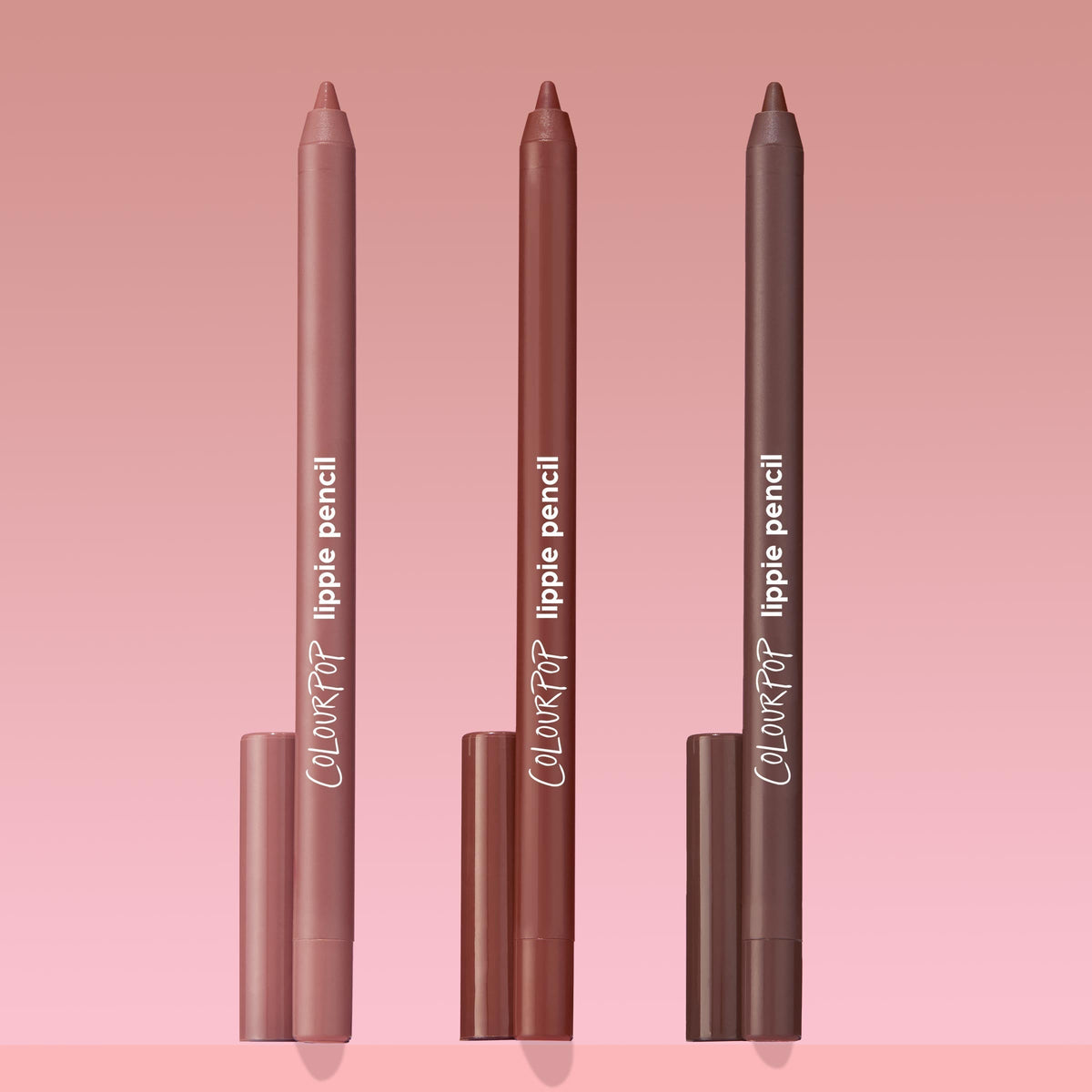 Triple Latte ColourPop Lippie Pencil trio standing upright, tips exposed, in light nude, warm rose-brown, and deep mocha shades with matching caps, showcasing creamy lip liners on a pink gradient background for precise lip shaping.
