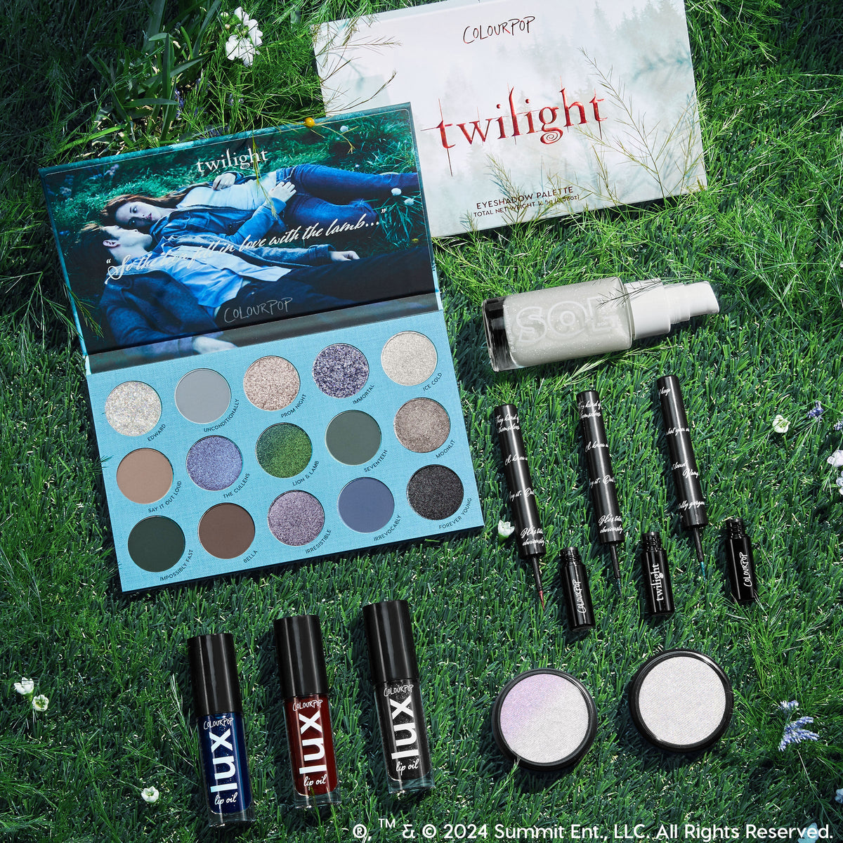 Twilight x ColourPop Full Collection arranged in a flatlay on grass with wildflowers, showcasing an open 16-pan cool-toned eyeshadow palette, black liquid liners, LUX lip oils, two iridescent highlighters, and a SOL body shimmer - ColourPop Full Collection Set.