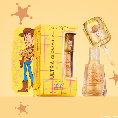 ColourPop Ultra Glossy Lip in Favorite Deputy shown open with the doe-foot applicator lifted, revealing a sheer gold sparkle gloss, the cap printed with Woody, beside a yellow Toy Story box on a warm yellow backdrop with sheriff stars.