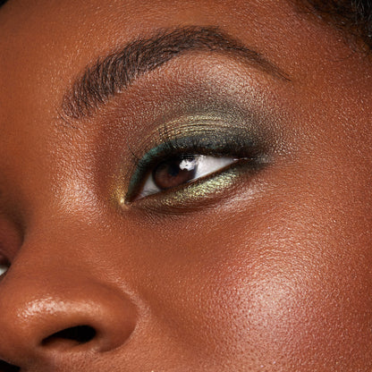 Eyelid wears ColourPop Moonwalk Super Shock Shadow, a duochrome olive-gold shimmer with green shift, blended across the lid and inner corner, highlighting metallic payoff and smooth finish in a close-up beauty swatch.