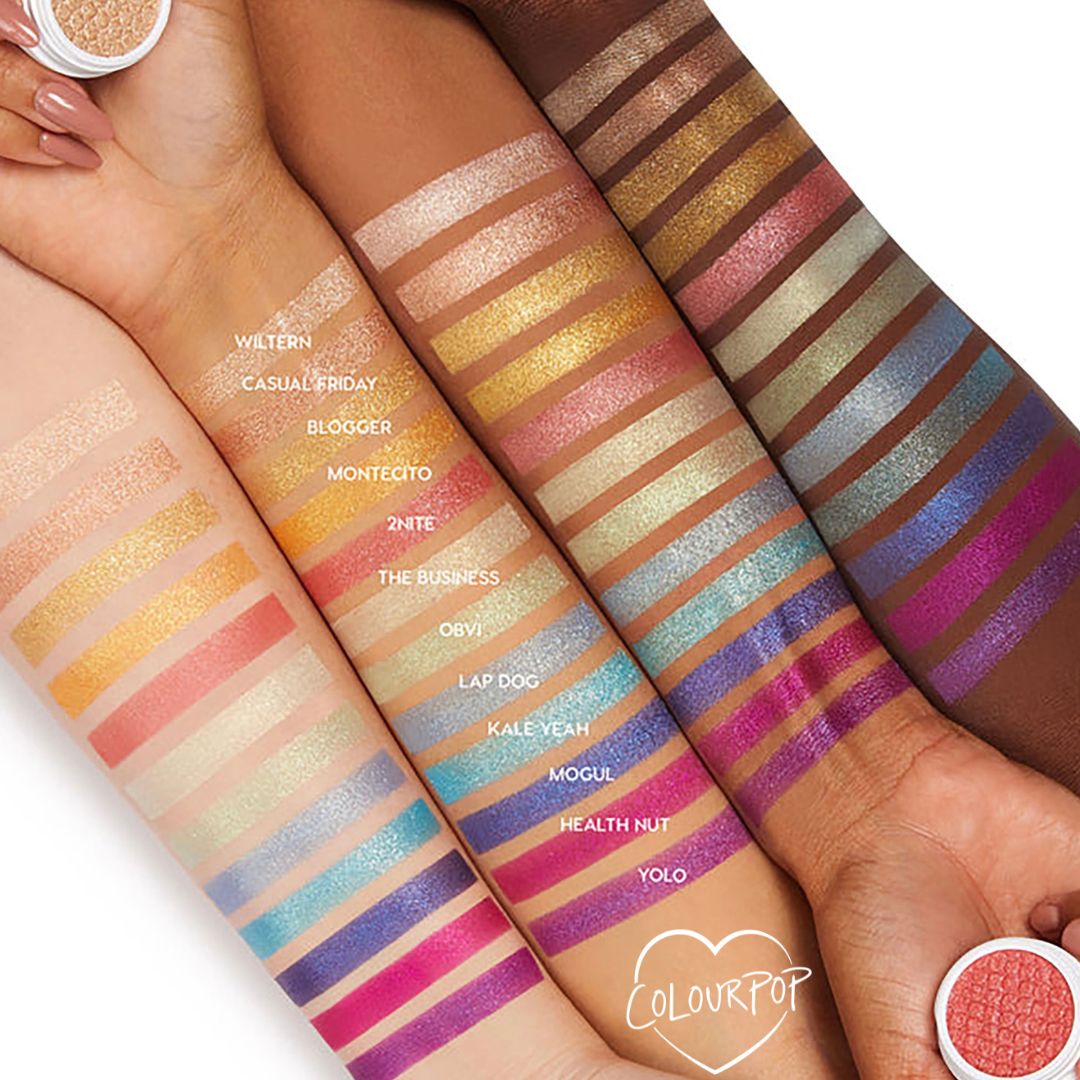 Obvi Super Shock Shadow by Colourpop swatched on multiple skin tones, showing its shimmery peachy-pink stripe among a rainbow of metallic Super Shock Shadow shades in an arm lineup, with small shadow pots framing the swatches.